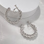 Silver twist hoop clip-on earrings displayed on white surface showing three angle views of the twisted design
