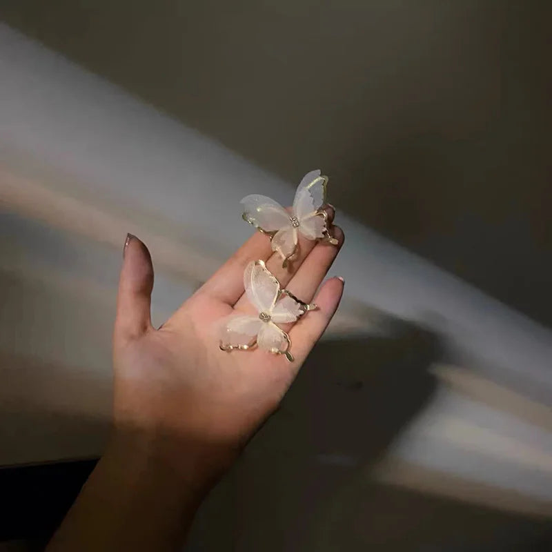 White butterfly wing clip-on earrings held in hand, showcasing delicate silhouette design with translucent pearlescent finish in natural sunlight