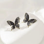 Black silhouette butterfly wing clip-on earrings with gold accents, displayed on white ceramic plate from above