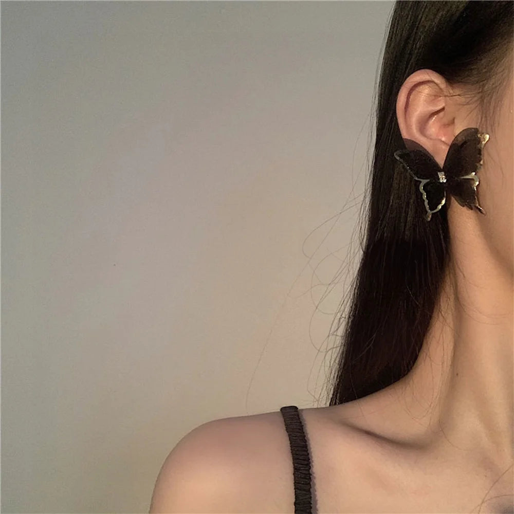 Black silhouette butterfly wings clip-on earrings worn on ear, side view showcasing delicate design and metal accents