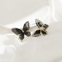 Black silhouette butterfly wings clip-on earrings displayed on white flower-shaped holder, front view