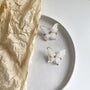 White silhouette butterfly clip-on earrings displayed on ceramic dish with crinkled paper, top view