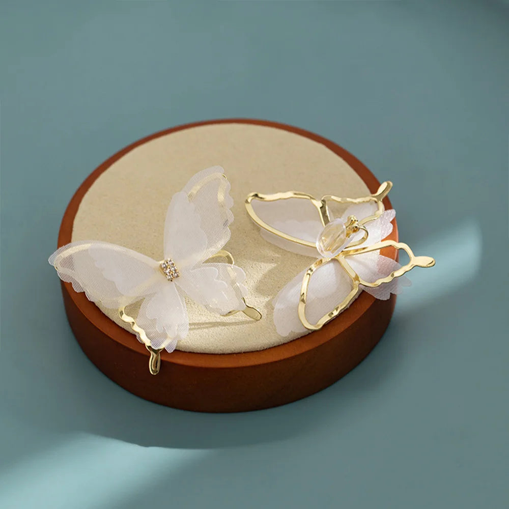 White butterfly clip-on earrings with gold accents displayed on cream jewelry dish against blue background