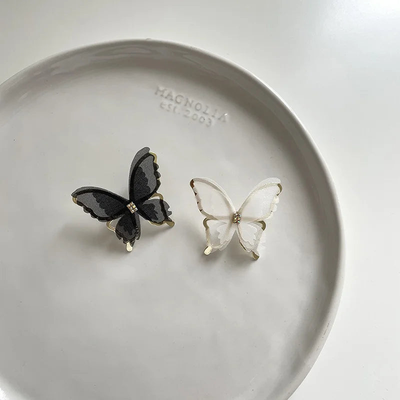 Black and white silhouette butterfly wings clip-on earrings displayed on ceramic dish, overhead view