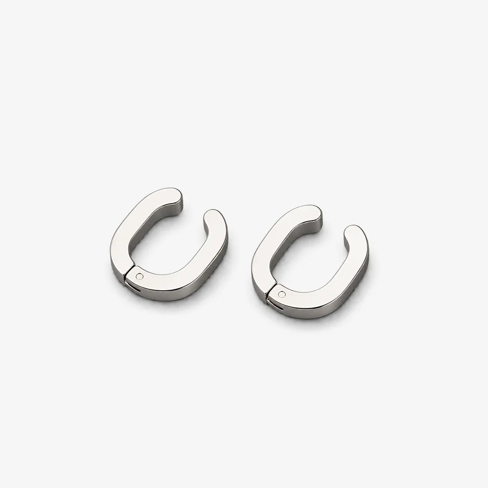 A pair of polished silver-toned metal hoop earrings with a unique rounded, open-ended design, displayed on a clean light gray background.