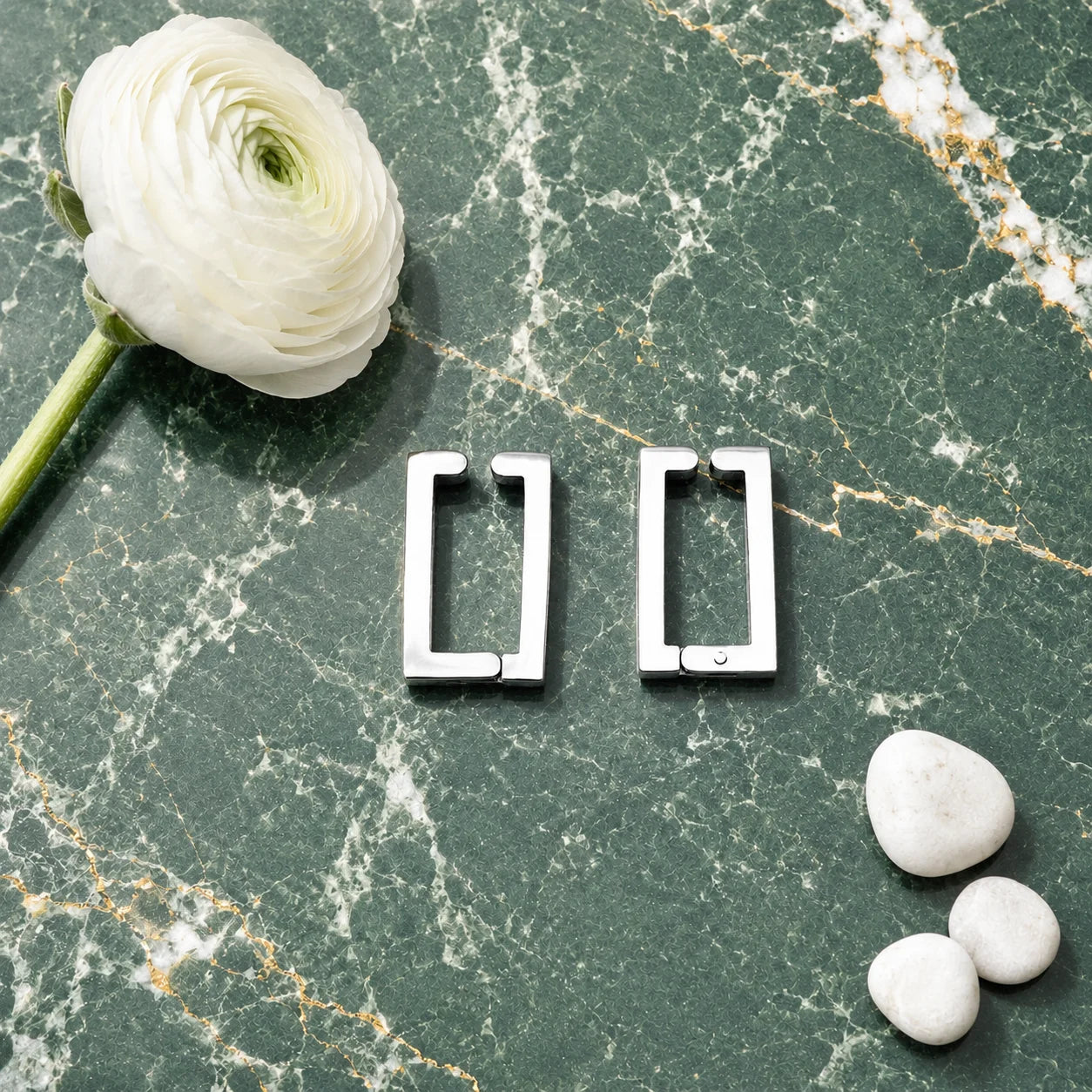 Silver rectangle clip on hoop earrings displayed on green marble surface with white flower and decorative stones