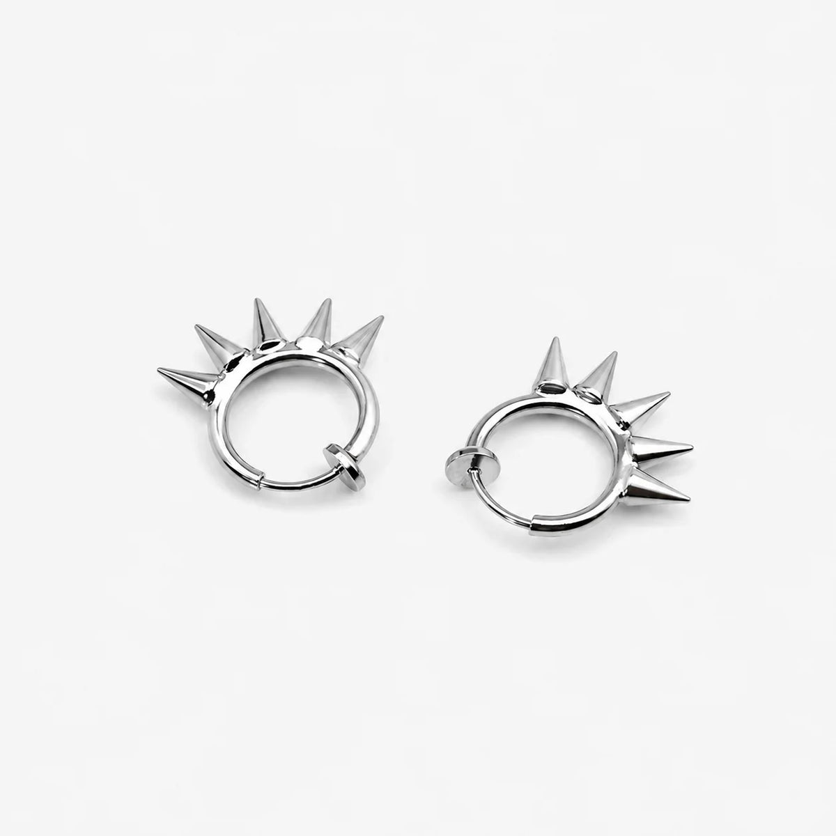 A pair of silver-toned spiky clip on hoop earrings on a clean, light gray background.