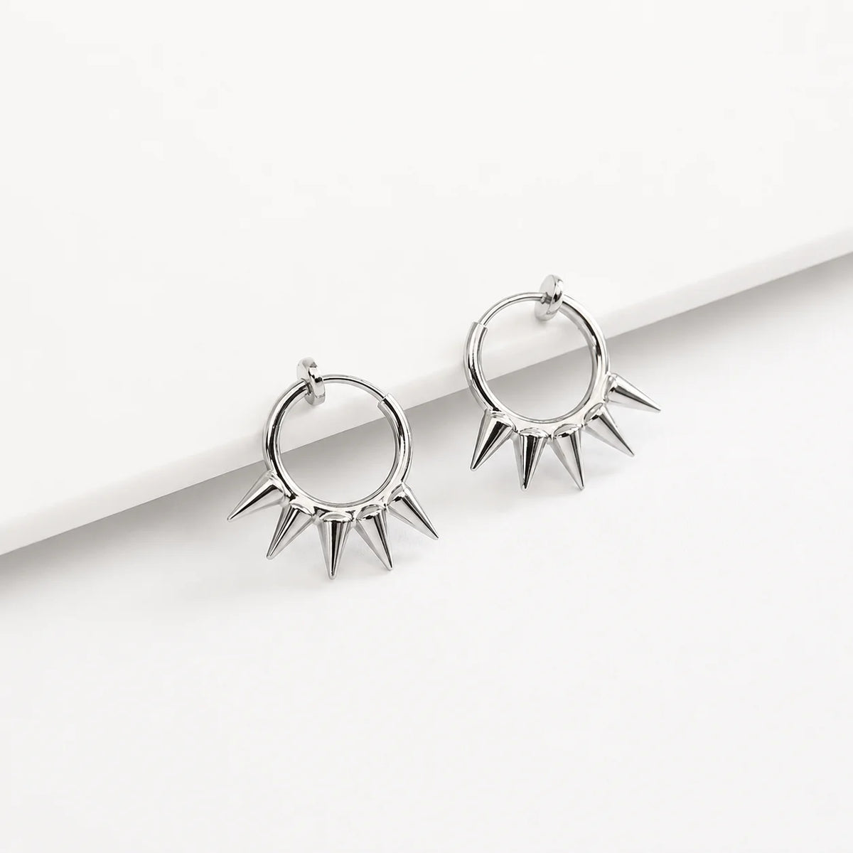 A pair of silver-toned hoop earrings with sharp spike details, displayed on a clean white surface.