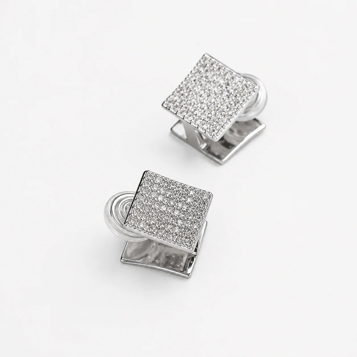 A pair of silver-toned square cufflinks, each featuring a pavé-set clear crystal face. The cufflinks are arranged diagonally on a clean, light off-white background.