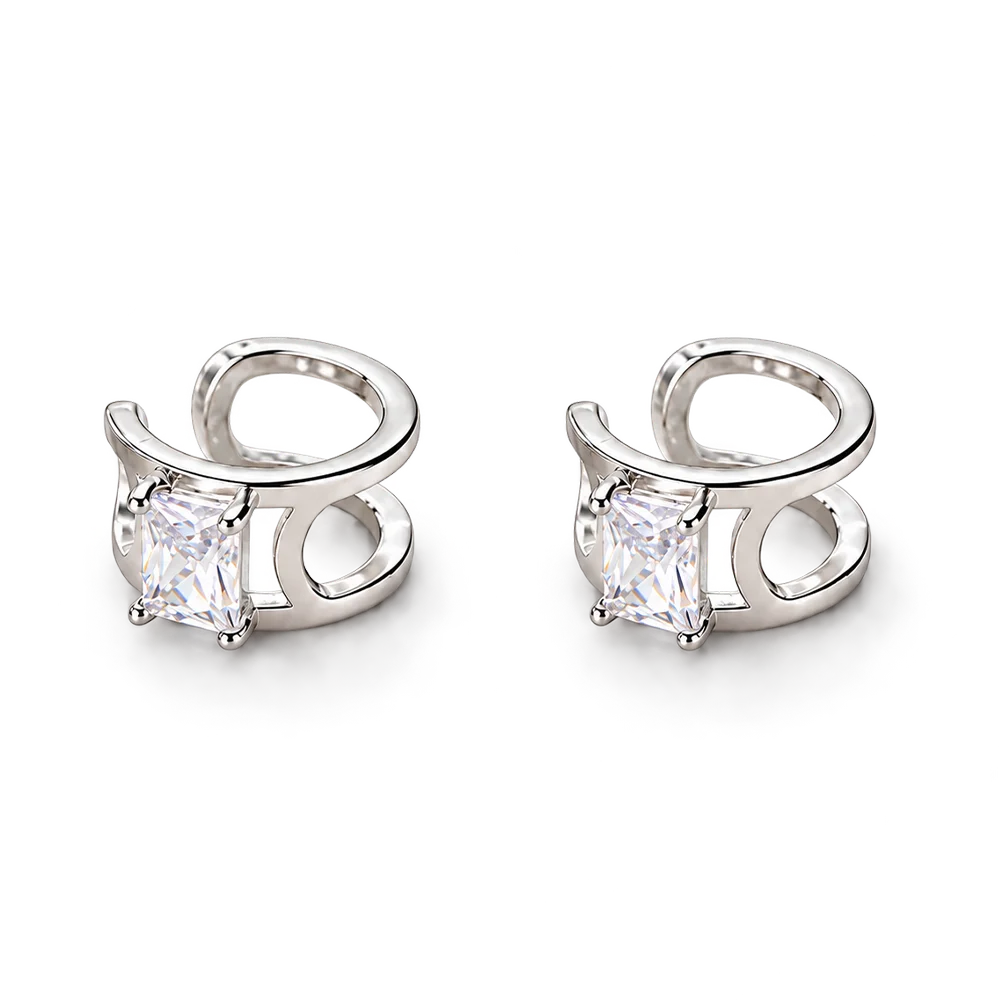 A pair of silver-toned huggie hoop earrings, each featuring a rectangular clear gemstone in a prong setting with a curved openwork metal design.
