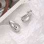 Silver chunky drop clip-on earrings displayed flat lay on white textured background showing polished finish detail