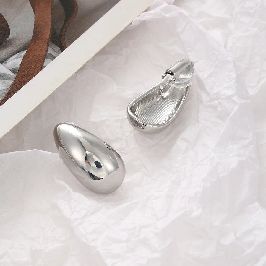 Silver chunky drop clip-on earrings displayed flat lay on white textured background showing polished finish detail