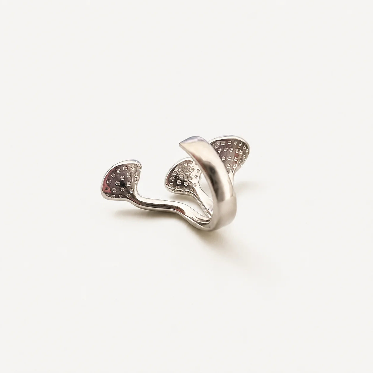 A silver-toned ring with a sculptural, organic shape and textured pavé-set details, photographed on a clean, light off-white background.