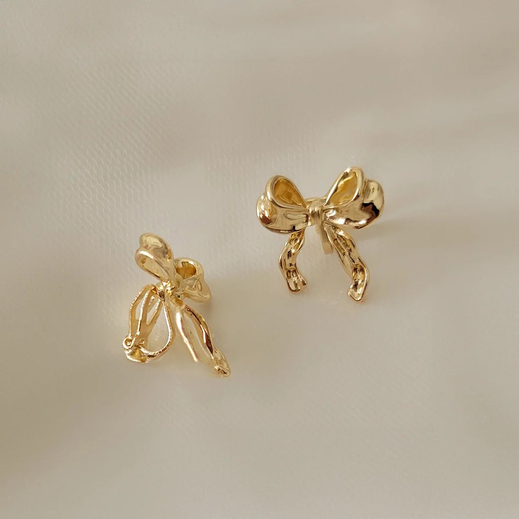 Gold simple bow clip on stud earrings displayed at angle on white background showing detailed design and shine
