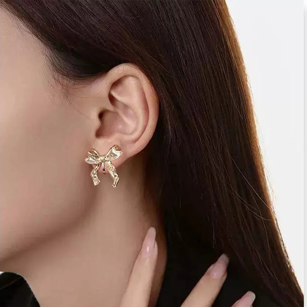 Gold simple bow clip on stud earrings worn on ear, side view showcasing textured bow design and metallic finish