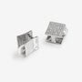 A pair of silver-toned square cufflinks on a light gray background. One cufflink is shown from the front, featuring a flat, polished metallic surface, while the other is turned to show the back, which has a textured, diamond-like pavé pattern on its top face.