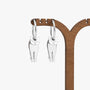 A pair of silver cat-shaped drop earrings hanging from a wooden jewelry display stand against a plain white background.
