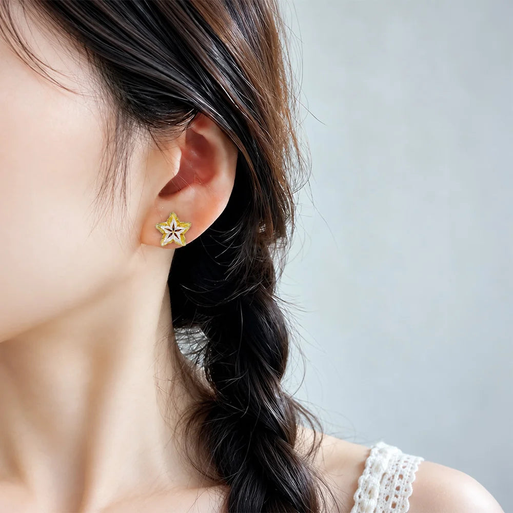 A close-up of a woman's ear wearing a small star-shaped stud earring with yellow, white, and gold detailing, set against a soft gray background.