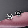 Silver lightning bolt magnetic stud earrings on pink fabric, angled view showing black and silver round design