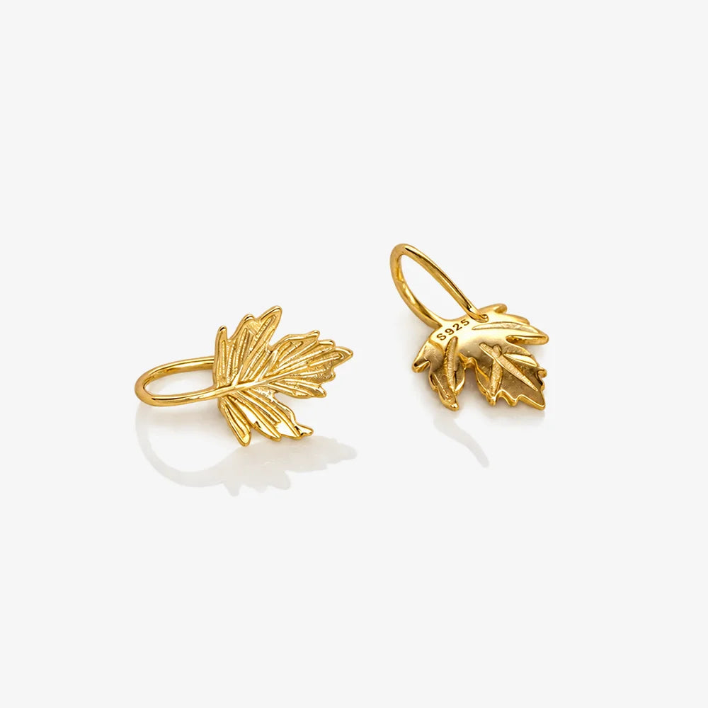 A pair of gold leaf-shaped hoop earrings on a clean, light gray background.