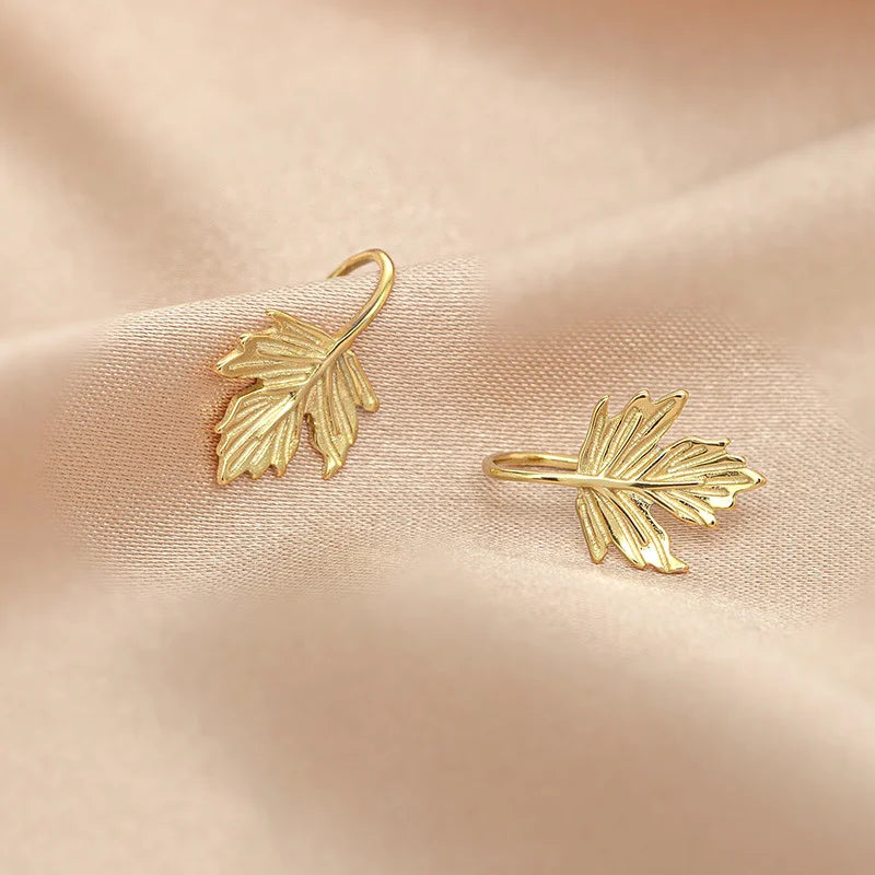 Pair of Sterling Silver Maple Leaf Cuff Earrings in Gold displayed on a soft pink fabric background.