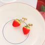 Strawberry Charm Clip-On Earrings in red and yellow displayed on white plate with gold hardware