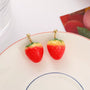 Strawberry charm clip-on earrings in red and gold displayed on white plate with red rim detail