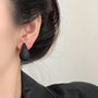 Black teardrop clip-on earrings side view worn on model with dark hair against neutral background