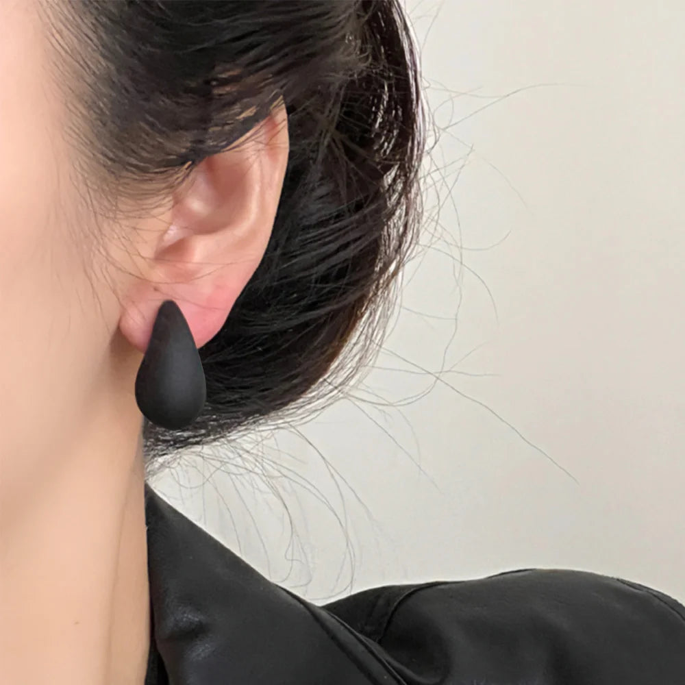 Black teardrop clip-on earrings side view worn on model with dark hair against neutral background