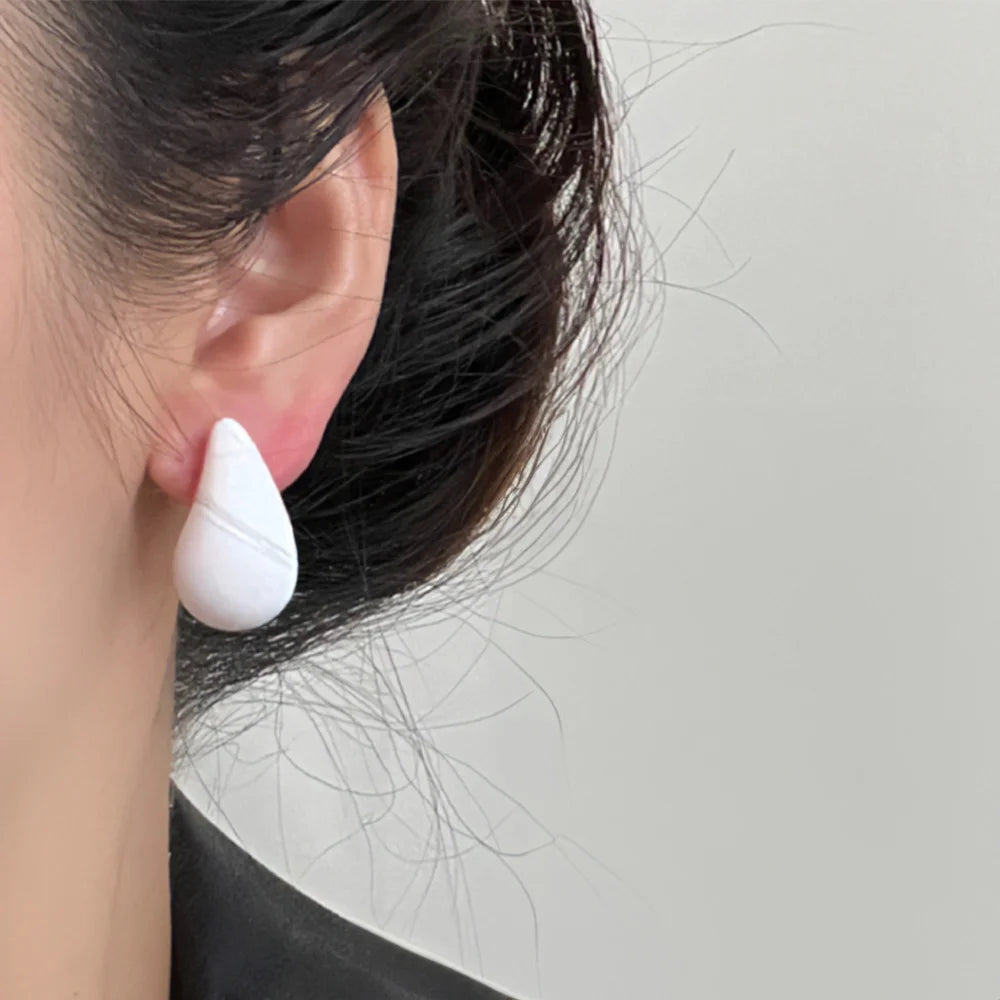 White teardrop clip-on earrings side view worn on ear with black hair against neutral background