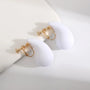 White teardrop clip on earrings with gold hardware displayed on white decorative stands, front view