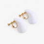 White teardrop clip on earrings with gold hardware displayed on white decorative stands, side view