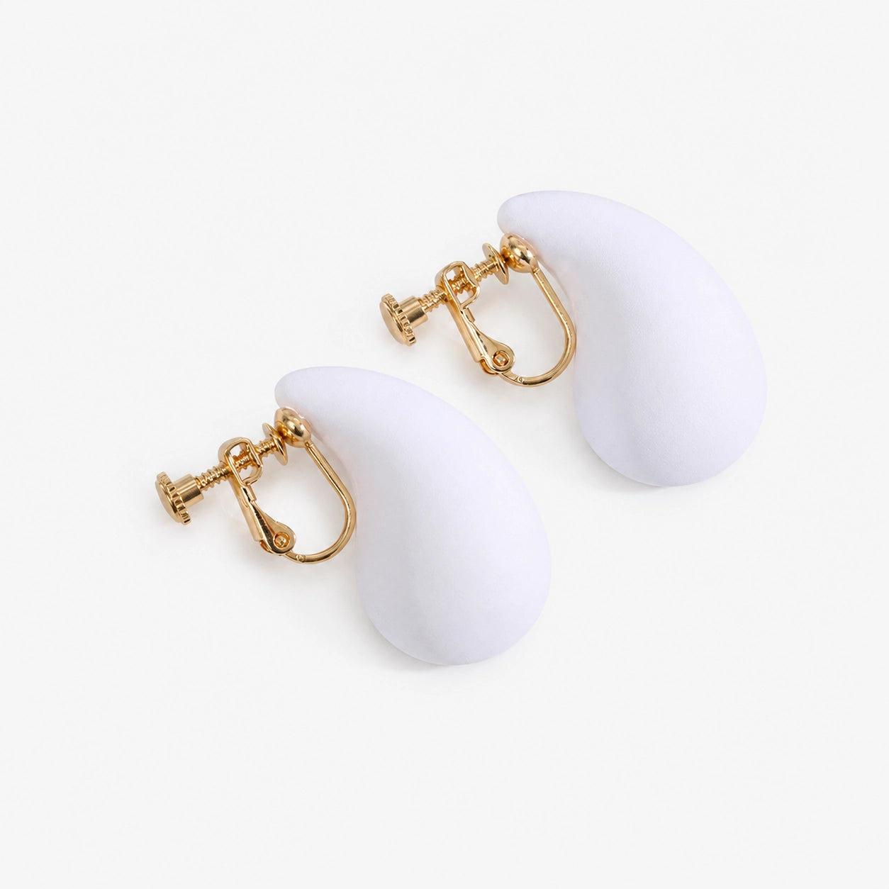 White teardrop clip on earrings with gold hardware displayed on white decorative stands, side view