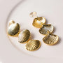 Gold textured shell clip-on earrings displayed on white surface showing detailed ridged design from above angle