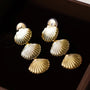Gold textured shell clip-on earrings displayed in set of six on black background, showing detailed ridged design from above