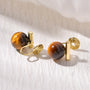 Tiger's Eye Clip On Earrings with gold spiral details, front view on white textured background