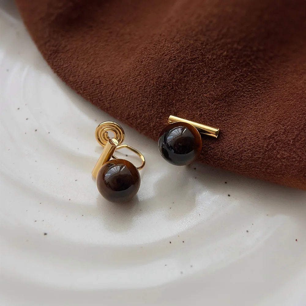 Tiger's Eye clip on earrings with gold accents displayed on white marble surface with brown fabric