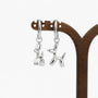 A pair of silver balloon dog hoop earrings hanging from a wooden display stand against a clean white background.