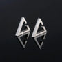 Pair of silver geometric triangle clip-on earrings with modern angular design, displayed at three-quarter view on dark background