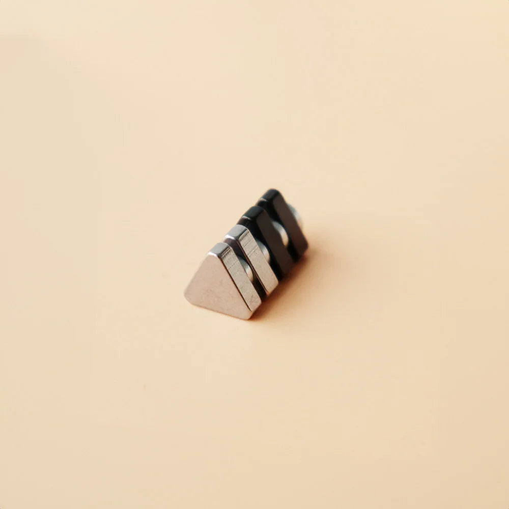 Triangle magnetic stud earrings in black displayed at an angle on a beige background showing the metallic and matte finish details