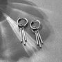 Silver triple rod tassel clip-on earrings flat lay on textured gray background