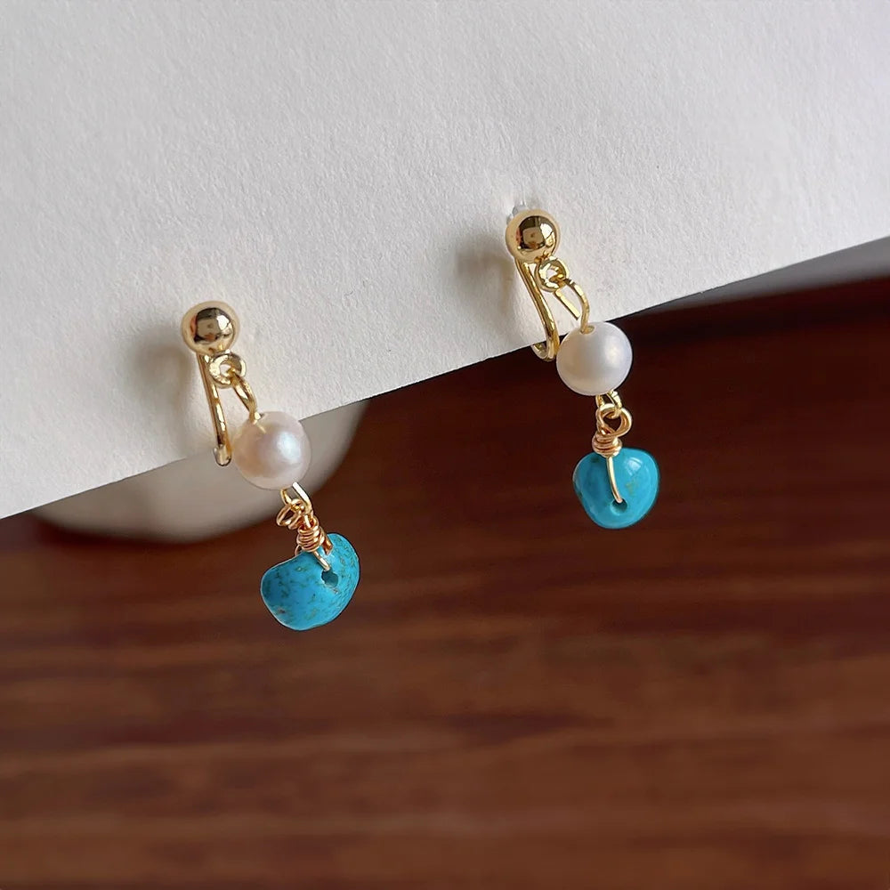 Turquoise clip on pearl earrings with gold accents displayed on wooden surface, front view