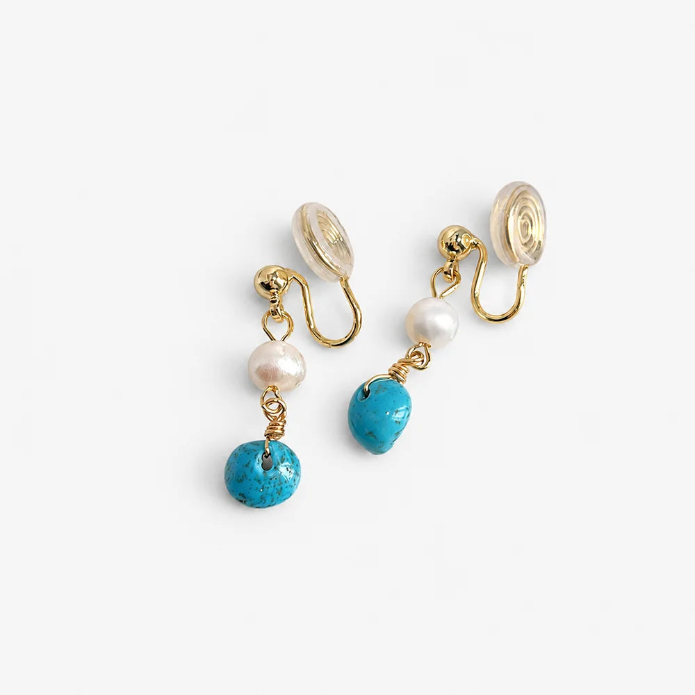 Turquoise clip on pearl earrings with gold hardware and clear silicone backing displayed on white surface