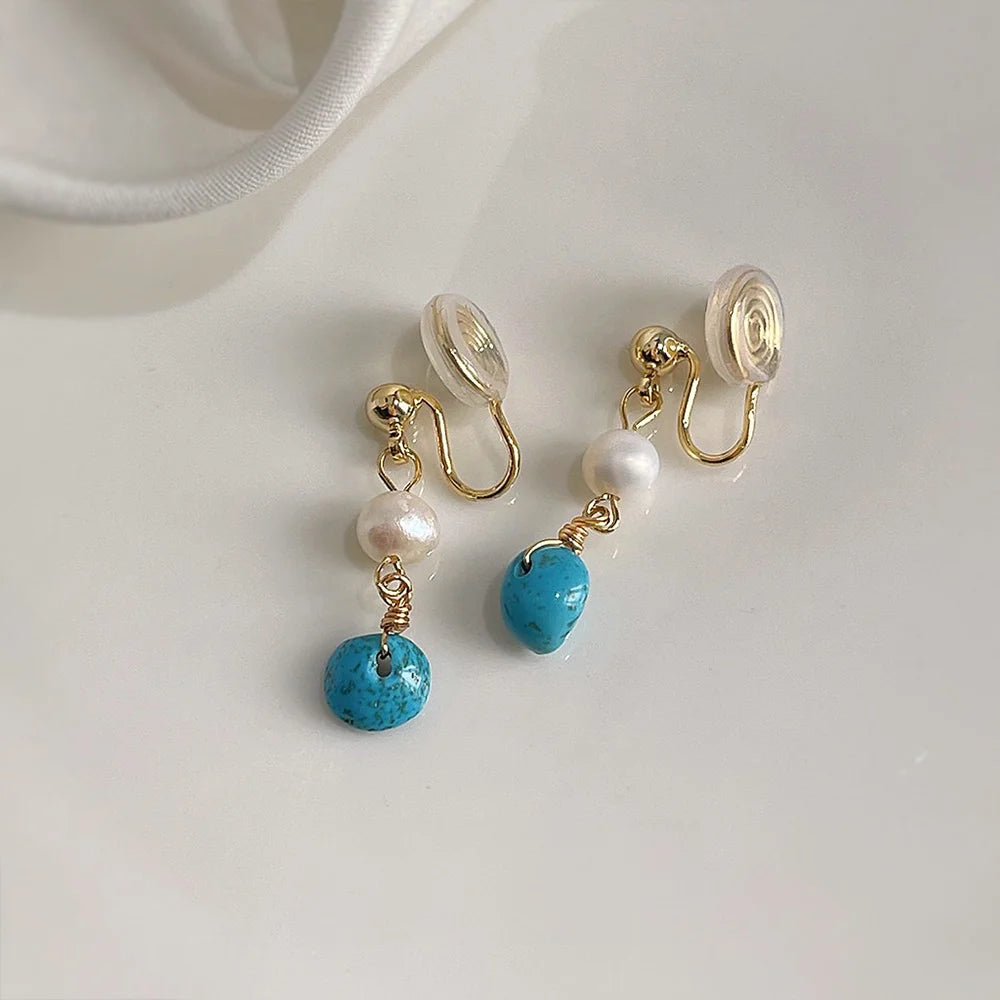 Turquoise clip on pearl earrings with gold hardware and clear silicone backing displayed on white surface