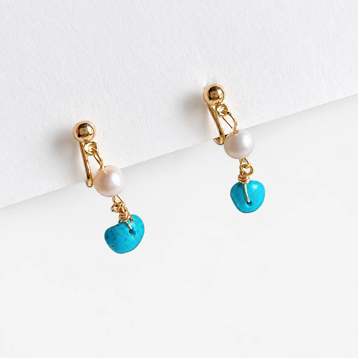 Turquoise clip on pearl earrings with gold accents clipping white paper