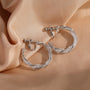 Silver glimmering lattice twist clip-on earrings displayed on ear model, showcasing textured design detail