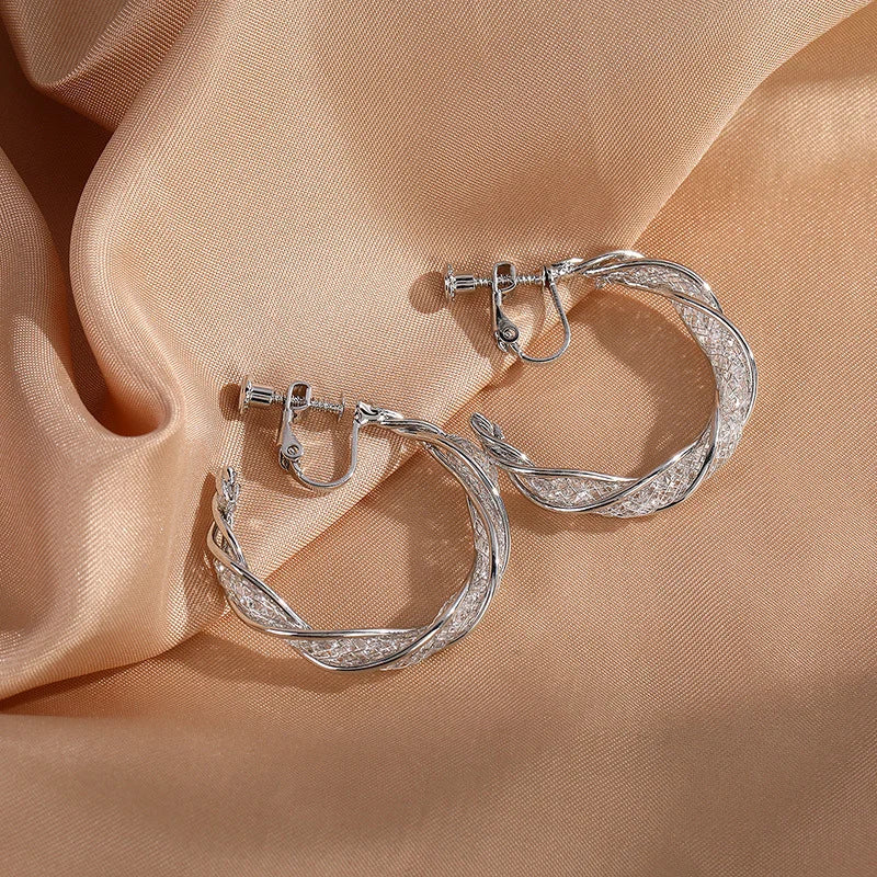 Silver glimmering lattice twist clip-on earrings displayed on ear model, showcasing textured design detail