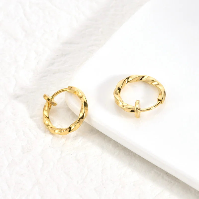 Pair of Twisted Huggie Clip On Hoop Earrings in Gold on a white background.