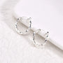 Twisted huggie clip on hoop earrings in silver displayed on white marble surface, angled view