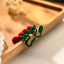 Velvet cherry clip-on earrings with red textured flowers and green stems, angled view on wooden surface